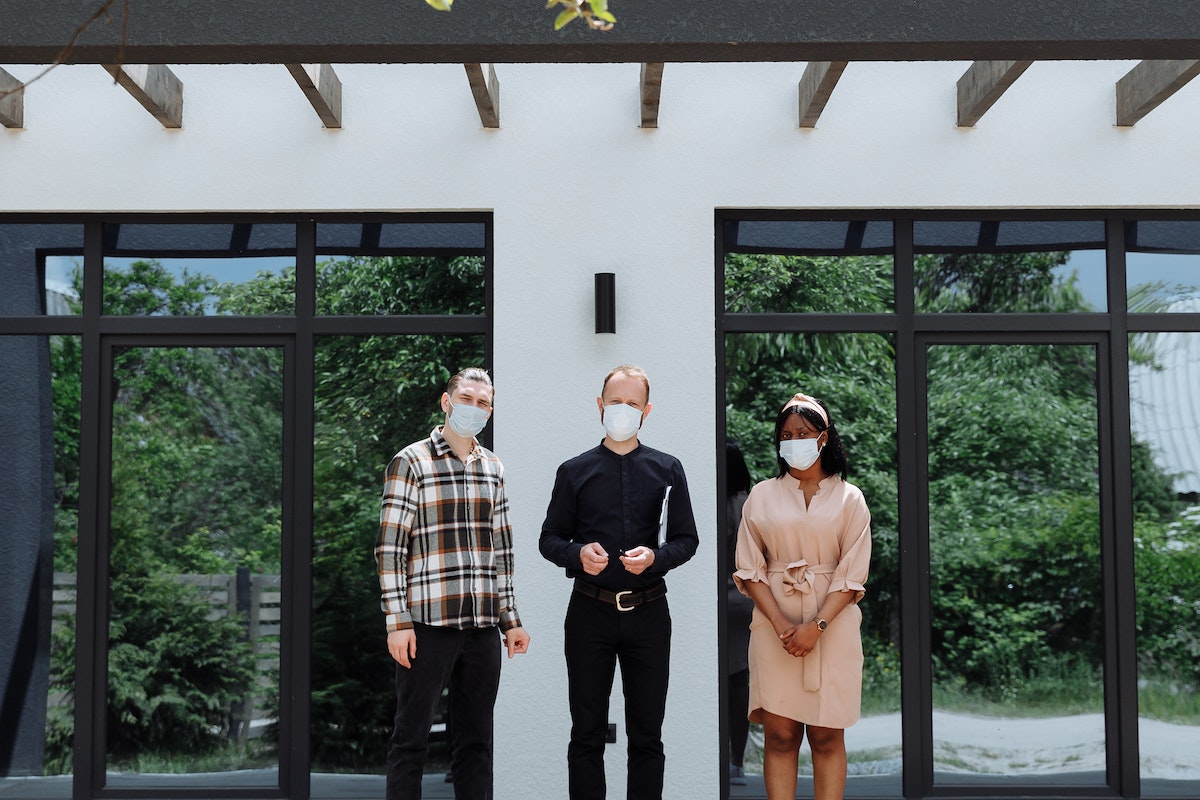 People-wearing-face-mask-standing-outside-an-elegant-house-while-looking-at-the-camera